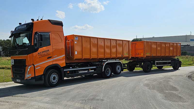 Oranger Aluminium Krüger LKW mit Anhänger auf dem Betriebsgelände, bereit für den Transport von Aluminiumschrott.