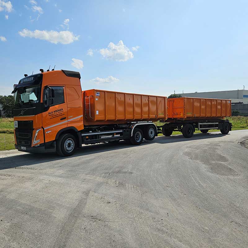 Oranger Aluminium Krüger LKW mit Anhänger auf dem Betriebsgelände, bereit für den Transport von Aluminiumschrott.