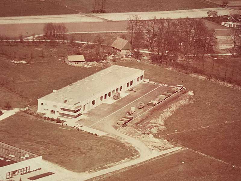 Frühe Luftaufnahme des ersten Aluminium Krüger Firmengebäudes in ländlicher Umgebung mit wenigen Fahrzeugen auf dem Hof