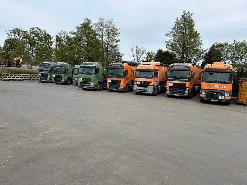 Reihe von grünen und orangefarbenen LKWs von Aluminium Krüger auf dem Betriebshof